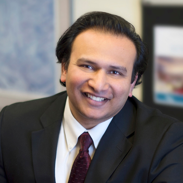 Amir Rizavi wearing a dark suit, yellow shirt and burgundy tie