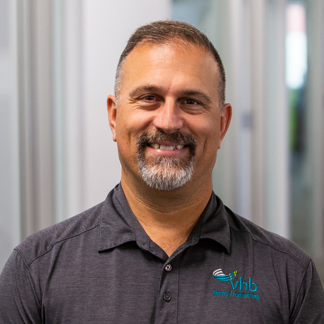 Bruce Marquis smiling in a VHB branded gray polo shirt.