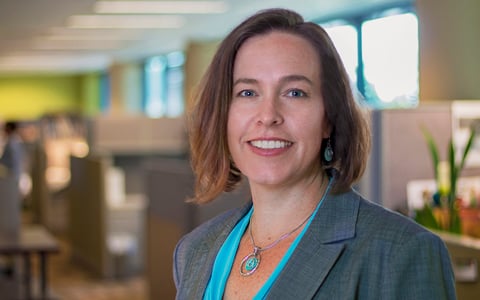 Amy Sirmans smiles while wearing a blue shirt and grey jacket.