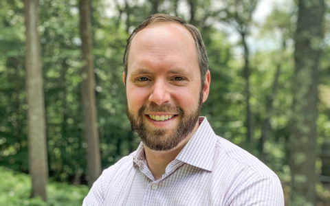 Andrew White in a pinstripe shirt standing in the woods 