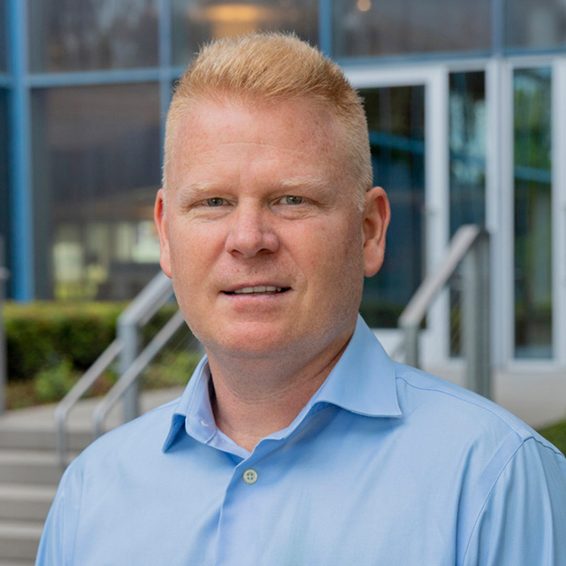 Greg Alban wears a blue collared shirt 