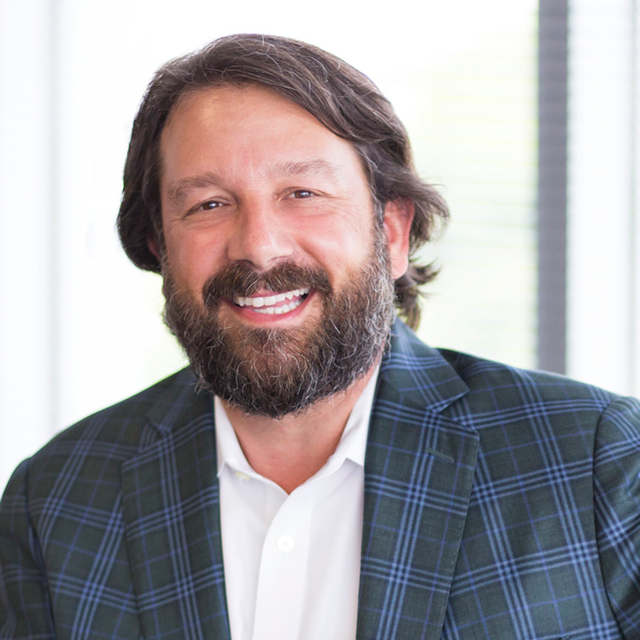 Kris Dramby, wearing a white shirt and plaid blazer, smiles in the office.