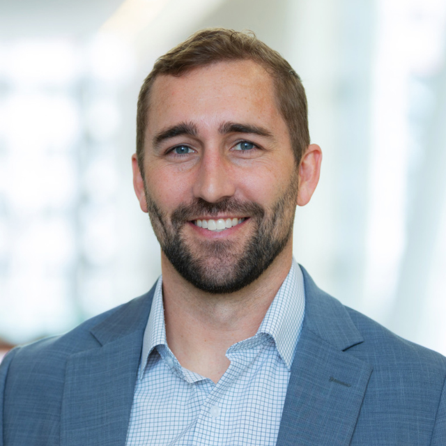 Seth at the office, wearing a white shirt and tan blazer.