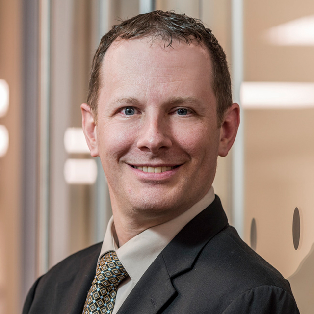 Tom Velleca in a dark brown suit and brown checkered tie