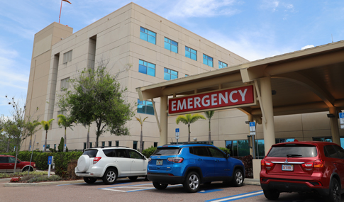 Red, white and blue SUVs parked in front of emergency room exit sign with exterior of hospital building in background at St. Joseph’s Hospital-South. 