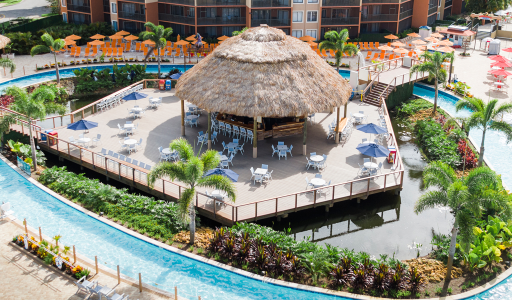 A cabana surrounded by lounging chairs, a lazy river, and greenery.