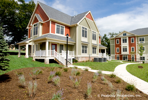 Green lawns in front of a red and grey apartment building. 