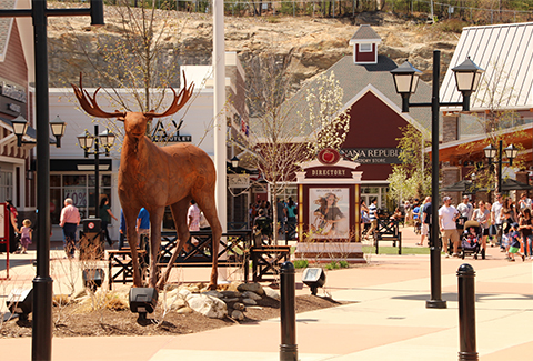 A moose statue stands is surrounded by several shops at the entrance of Merrimack Premium Outlets.