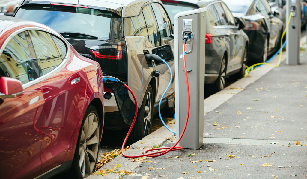 Electric vehicles plugged into charging stations along a city street.