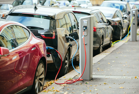 Electric vehicles plugged into charging stations along a city street.