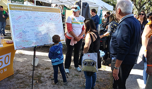 A child writes his thoughts for the future on a StPete2050 Vision whiteboard.