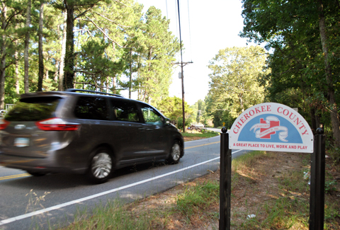 A gray minivan passes by a Cherokee County welcome sign.