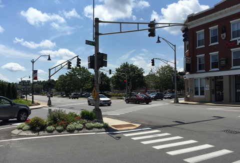 Cars pass under multiple traffic signals at an intersection in front of a brick building.