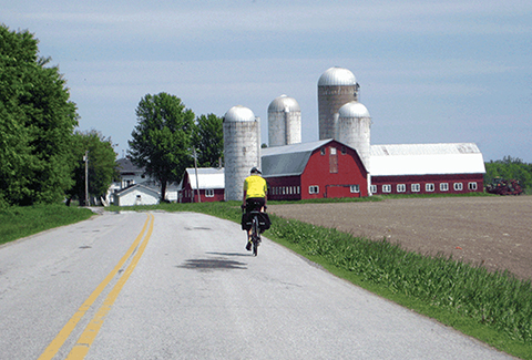 A bicyclist on a rural Vermont road near a red barn.