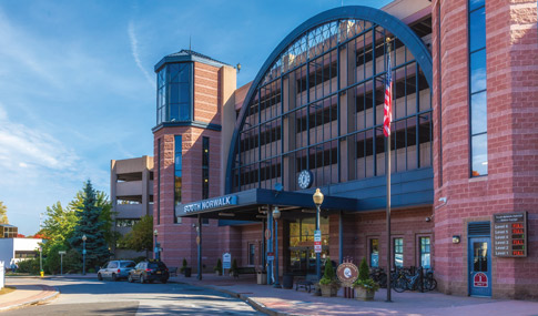 The westbound entrance to the South Norwalk train station and its parking garage, with cars parked outside.