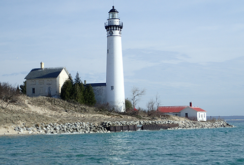 A lighthouse and attached cottage sit next to a rocky shoreline on the ocean.