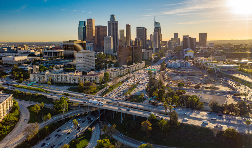 Aerial view of LA skyline with skyscrapers and freeway traffic below.