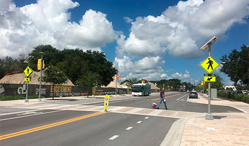 Man in a street crosswalk with yellow signs and an oncoming bus in the other lane. 