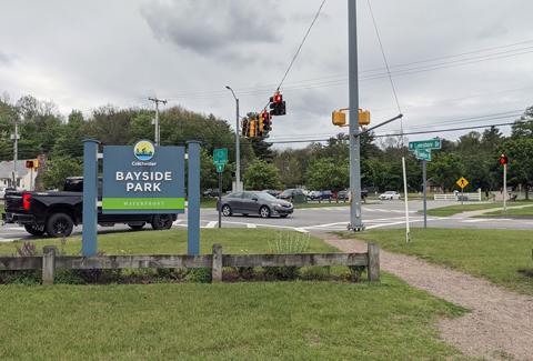 A grassy, signalized intersection with street signs and multiple vehicles visible on the road.