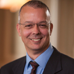 A smiling man wearing glasses and a suit