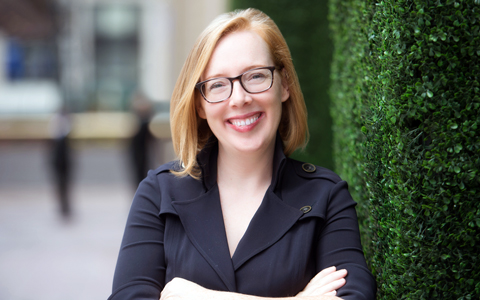 Allison Ruddock leaning against a green wall wearing a black jacket.