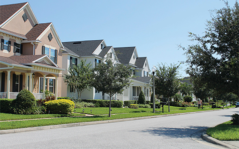 A view of a suburban street with new two-story houses and recently planted trees in the yards