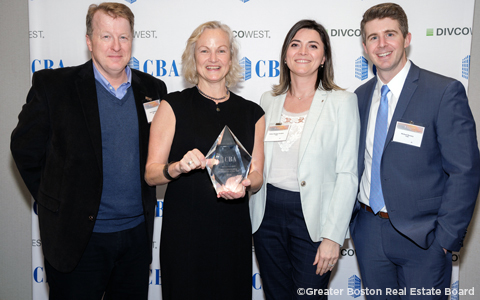 Four people stand with an award in front of a white banner.