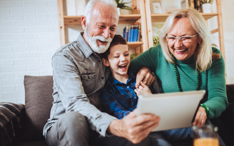 Young boy and grandparents sitting on couch looking at tablet.