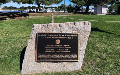 A cement path leading to the waterfront in Newburyport. A plaque on a stone next to the path reads, ”Market Landing Park Expansion, City of Newburyport 2024.