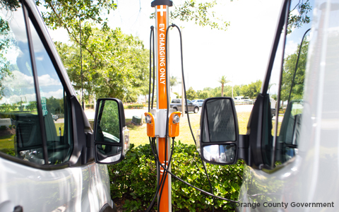 Two white vans are plugged in to an electric vehicle charging station outside