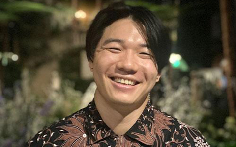 Tufts University Student, Erwin Li, stands outside smiling big with a black and maroon floral button-down shirt. 