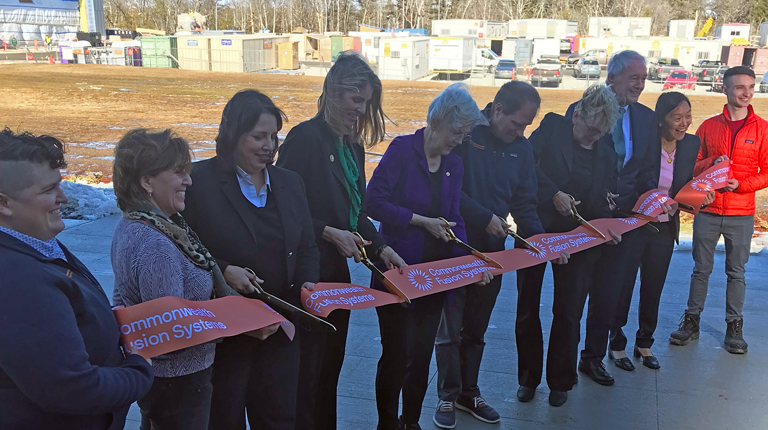 People standing outside cutting a red ribbon in an industrial park.