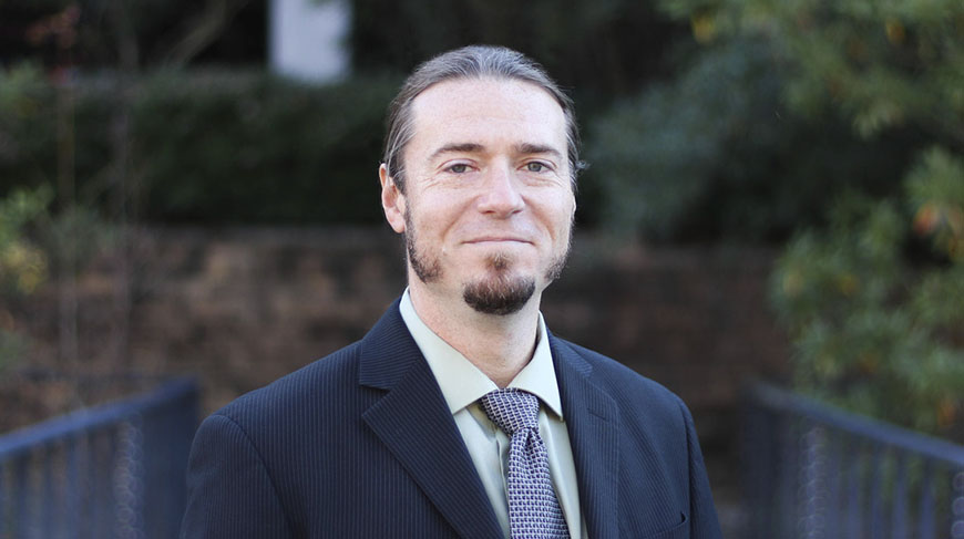 David Cooper smiles at the camera wearing a suit and tie.