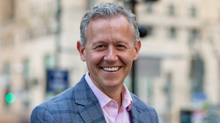 David Quart smiling in a blue suite and pink shirt.