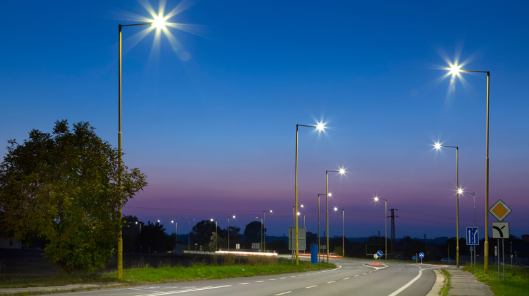 Street lights light up the evening sky at a turn on suburban road lined by trees