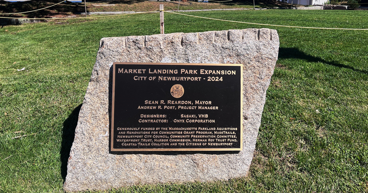 A cement path leading to the waterfront in Newburyport. A plaque on a stone next to the path reads, ”Market Landing Park Expansion, City of Newburyport 2024.