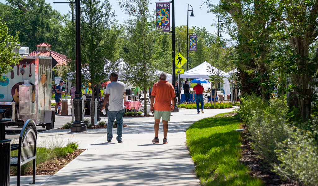 People walk on a park sidewalk with food trucks nearby