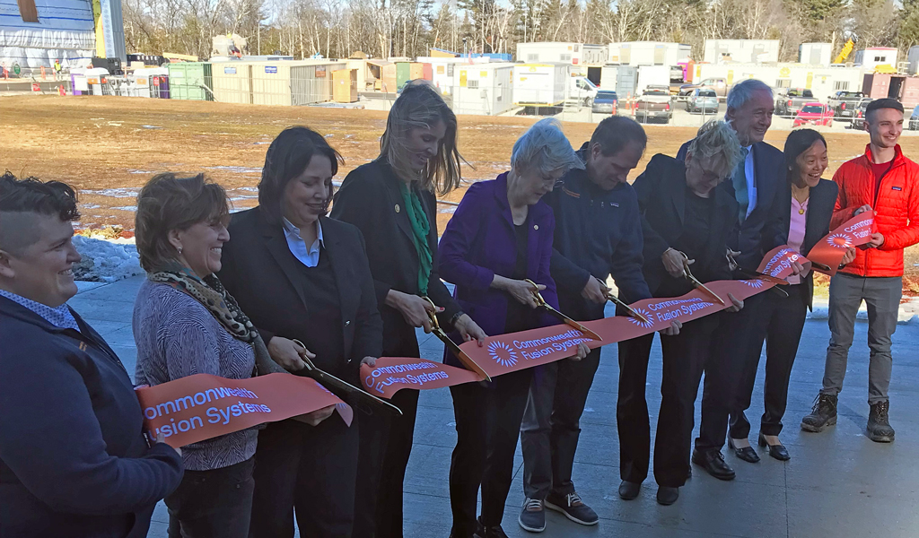 People standing outside cutting a red ribbon in an industrial park.