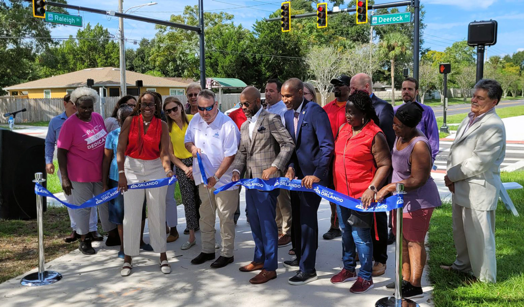 A group of people behind a blue ribbon cutting ceremony on a path.