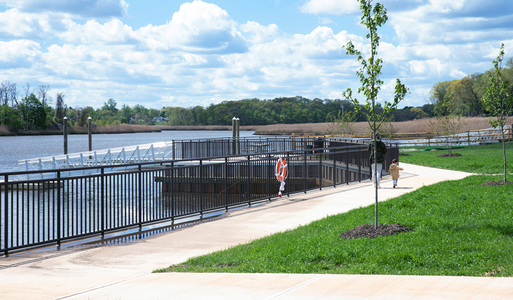 A waterfront walkway with a fence and grass.