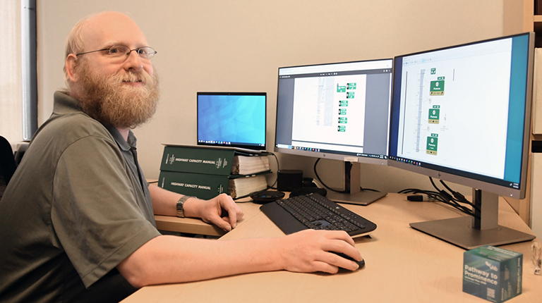 Michael Tantillo in a green shirt work on traffic signage designs across three computer screens.