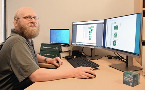 Michael Tantillo in a green shirt work on traffic signage designs across three computer screens.