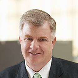 Mike McArdle smiling in the office wearing a suit and tie.  