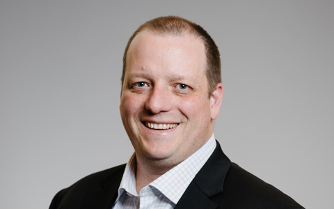 Francois Valois smiles while wearing a white shirt and dark jacket.