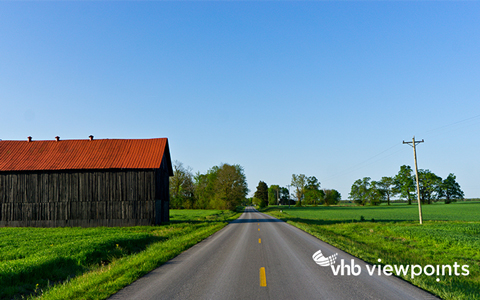 A road in a rural area surrounded by hills, greenspace and a barn