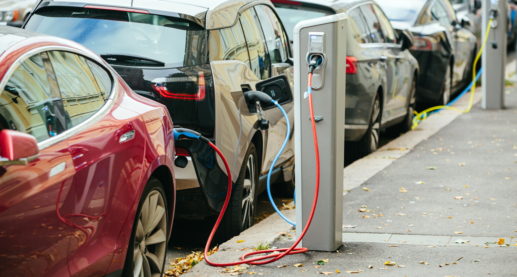 Electric vehicles parked curbside and connected to charging stations.